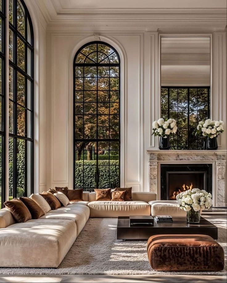 Elegant living room with tall arched windows, marble fireplace, and a large cream sectional sofa.