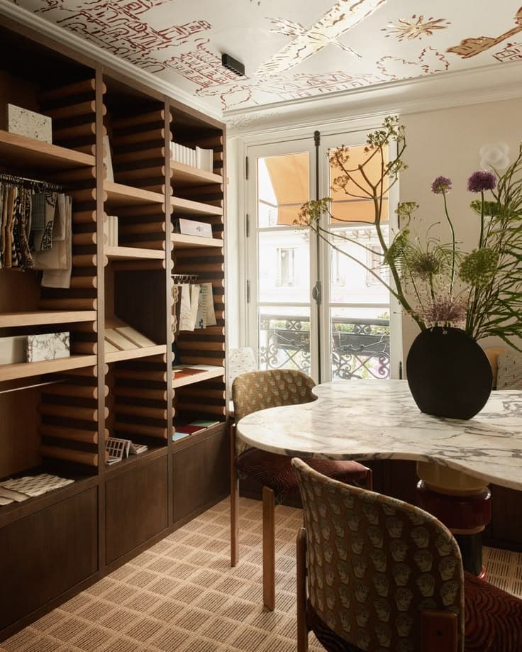 Marble table and black vase in a room with wooden shelving and an illustrated ceiling.