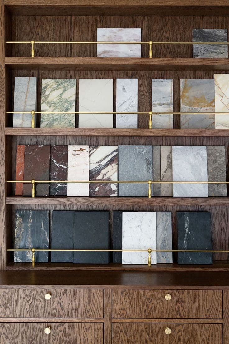 Various marble and stone samples displayed on dark wood shelves with thin brass railings.