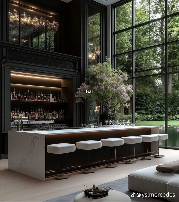 Modern marble bar with white stools and large windows overlooking a lush green garden.