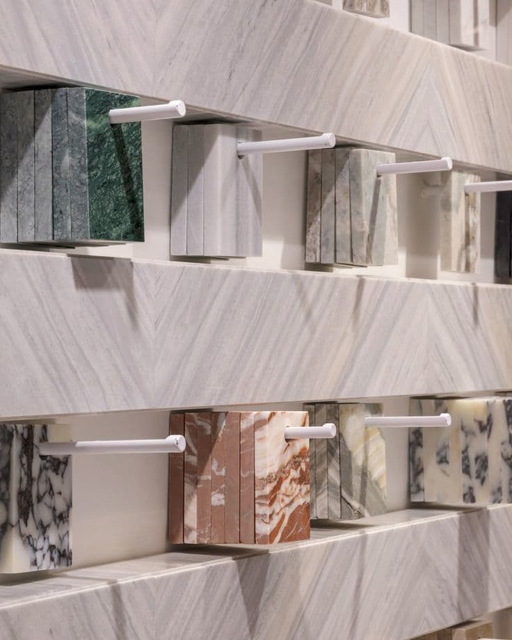 Various marble and stone samples hanging on white pegs against a chevron-patterned marble wall.