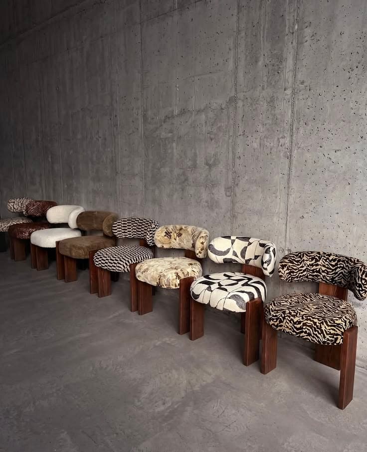Modern chairs with various patterned upholstery and wooden legs lined against a concrete wall.