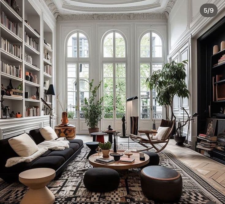 High ceilinged living room with floor to ceiling bookshelves, large arched windows, and modern furniture.